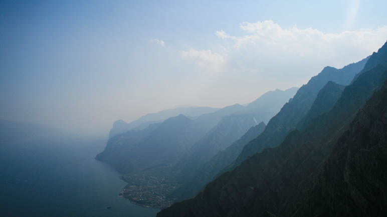 Die Berge des westlichen Gardasee-Ufers verlieren sich im Dunst. Unten am Ufer sieht man den Ort Limone.