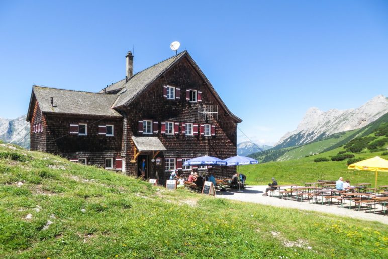 Die Falkenhütten steht auf einer Anhöhe inmitten von Wiesen vor der Laliderer-Felswand