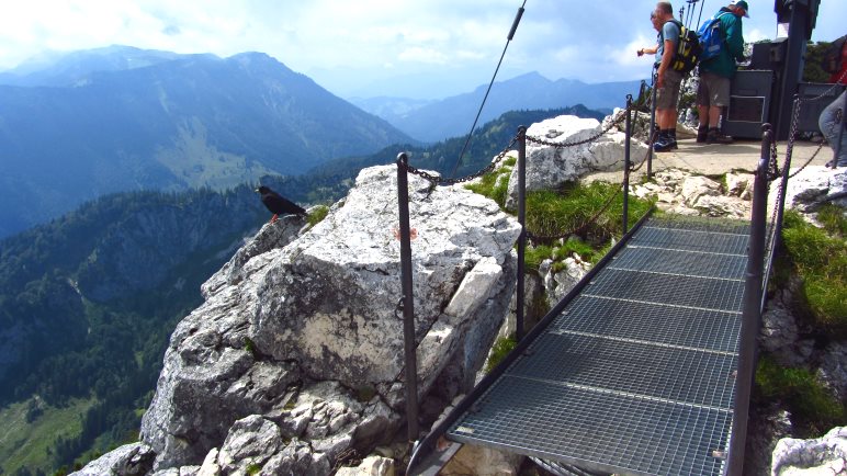 Über die kurze Brücke geht es zum 12 Meter hohen Gipfelkreuz der Kampenwand