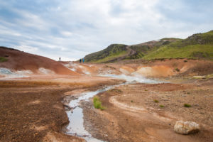 Wie aufgerissen wirkt die Landschaft am Seltún. Darüber die grünen Hügel