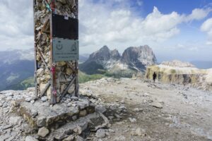 Das Gipfelkreuz des Sass Pordoi. Im Hintergrund die Langkofel-Gruppe und rechts der Piz Ciavazes
